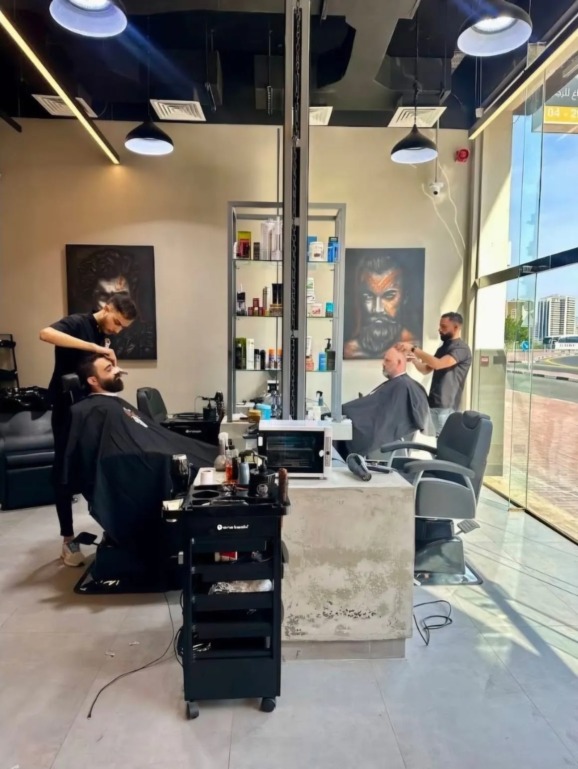 Inside Qaser Alanaqa: two barbers at work, a product shelf between the stations and tall windows onto 44th Street