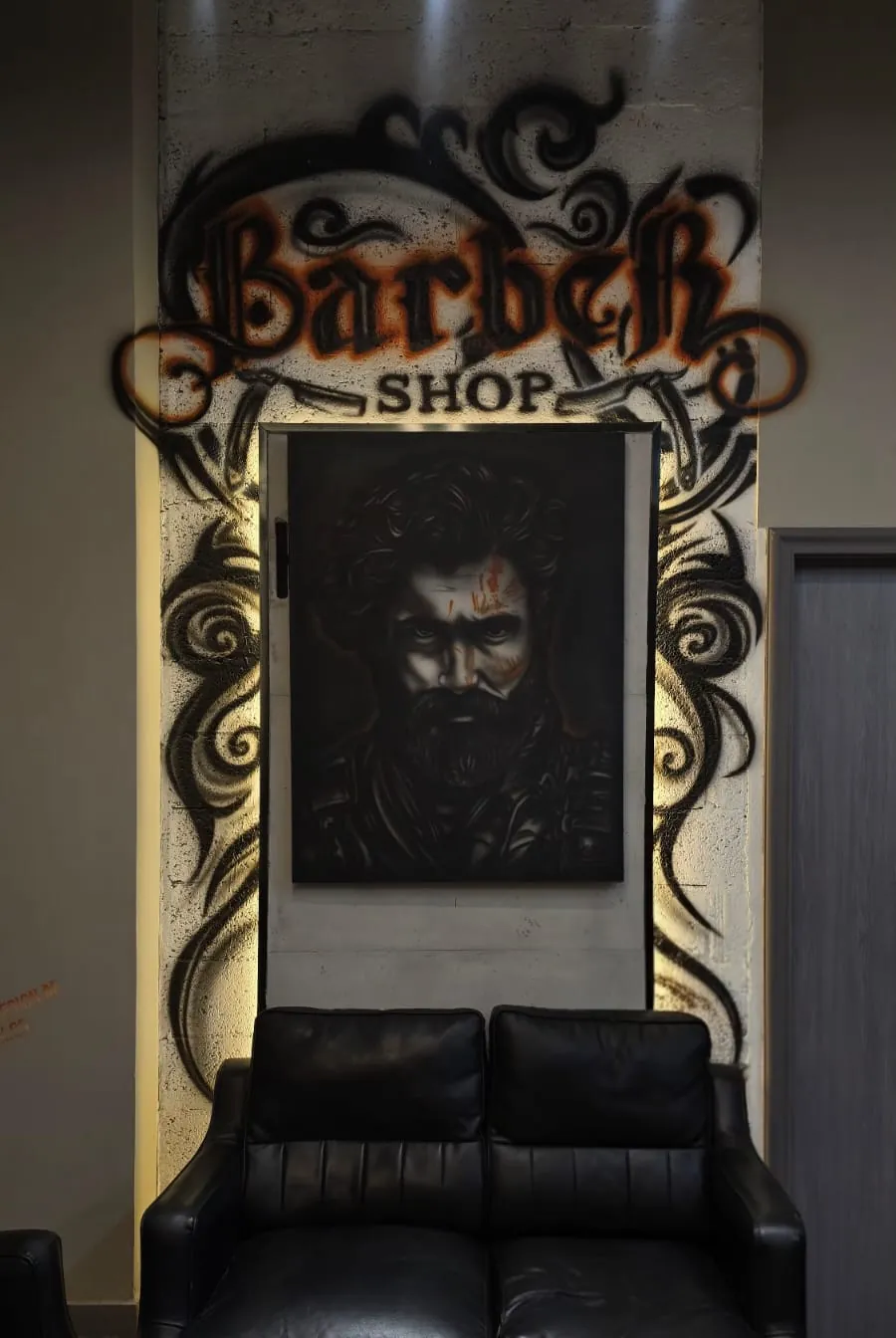 The salon's lounge: a black leather sofa beneath a hand-painted Barber Shop mural and a bearded portrait